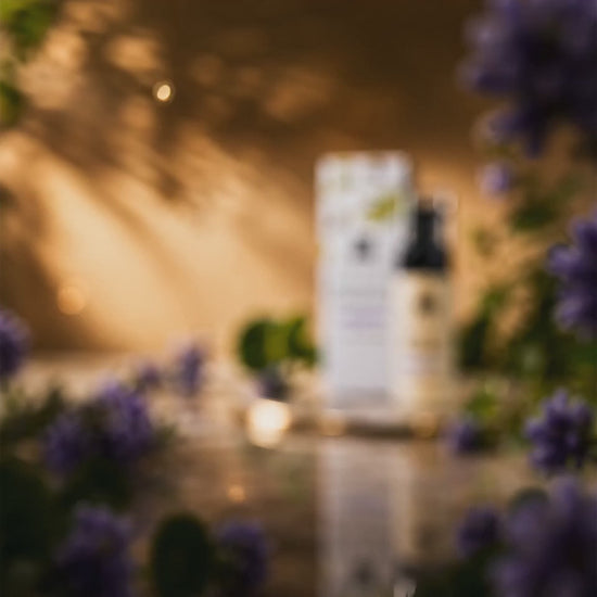 "Product video for DEHAZ Retinol & Centella Renewing Cream: close-up shots of the cream's texture and pump dispenser, styled with Centella Asiatica leaves and purple flowering botanicals on a marble and gold surface, jar and box rotating to display label, ending on a lifestyle shot of a model with smooth, radiant-looking skin."
